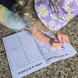 Child wearing a purple floral hat and sitting on the ground with a australian road trip coloring book.