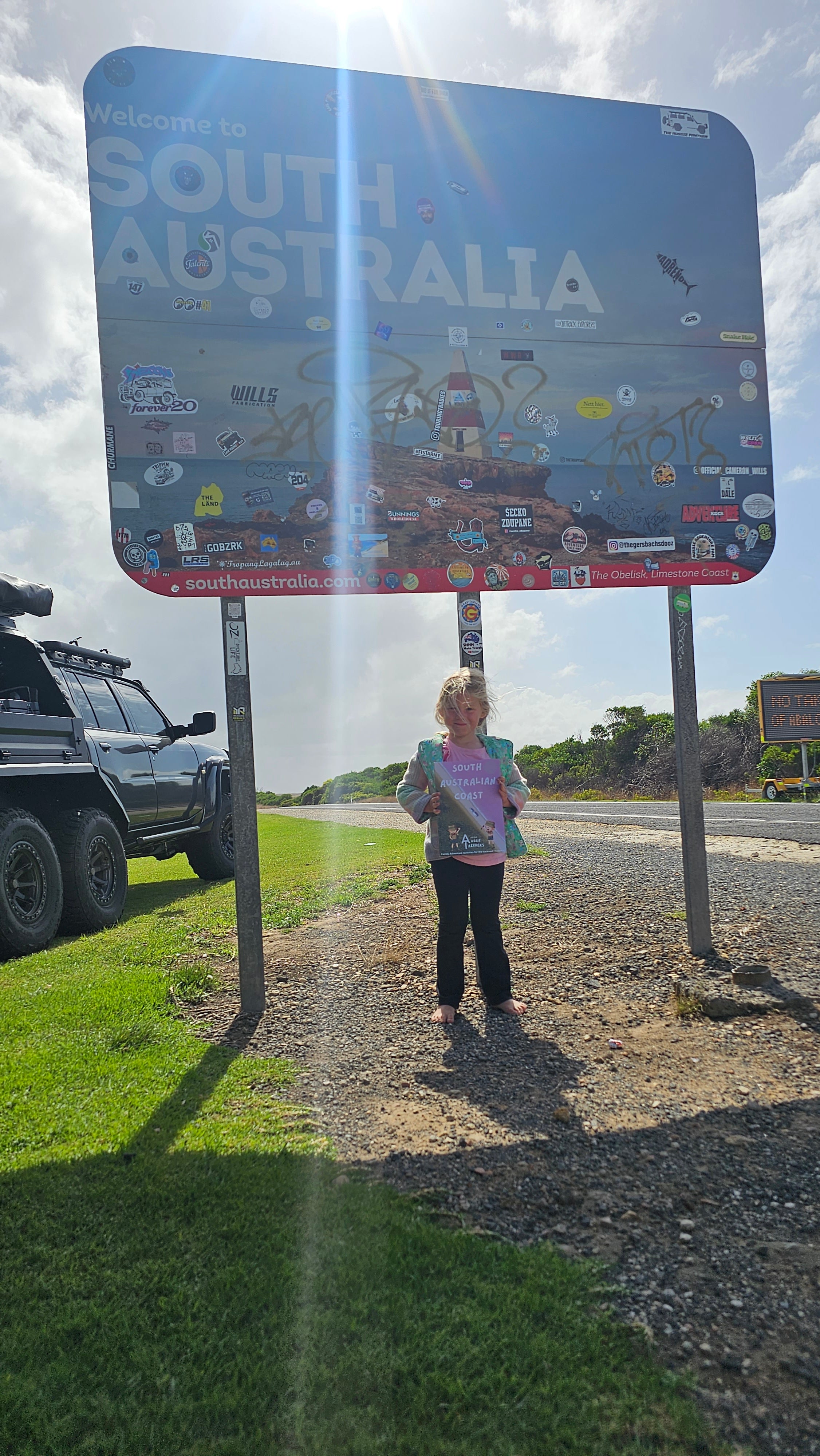 Child with south australian travel ournal in front of state boarder sign