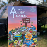 A colorful travel journal titled 'Kids Australian Travel Journal' being held in front of a camping backdrop.