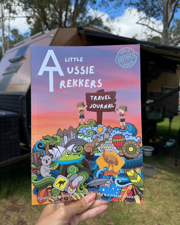 A colorful travel journal titled 'Kids Australian Travel Journal' being held in front of a camping backdrop.