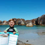 young boy holding up travel journal in front of elephant rocks
