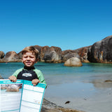 young boy holding up travel journal in front of elephant rocks
