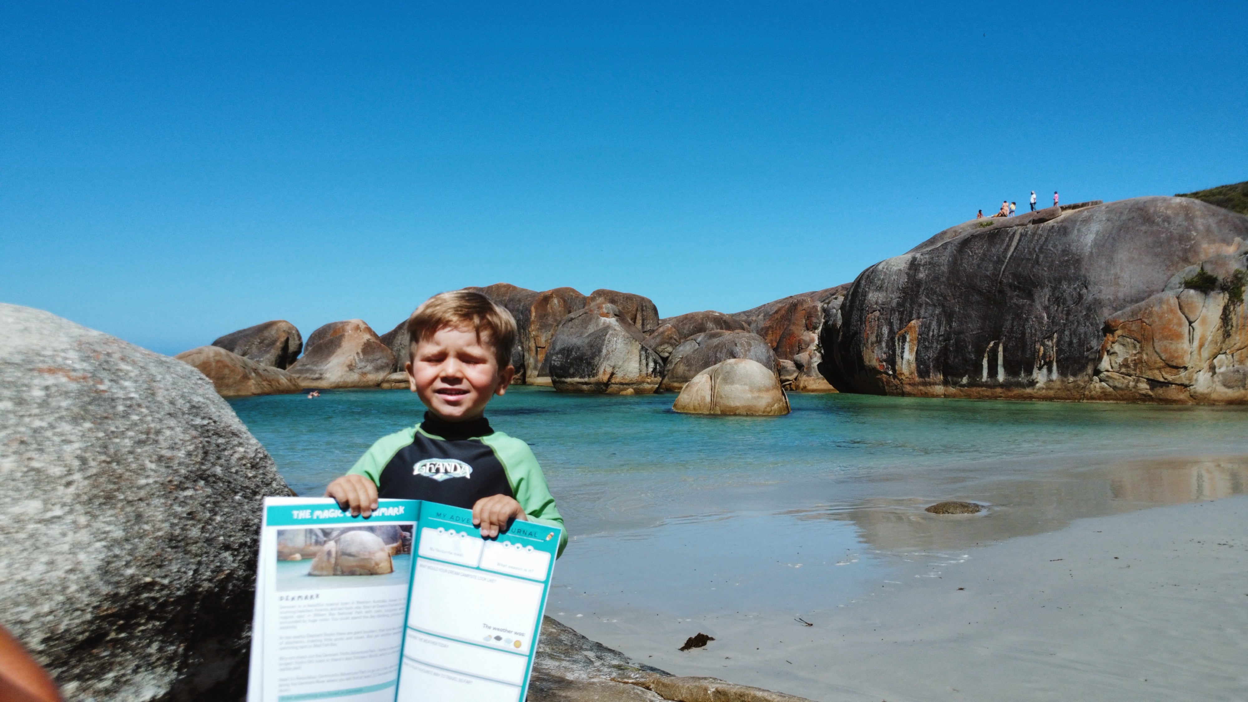 young boy holding up travel journal in front of elephant rocks
