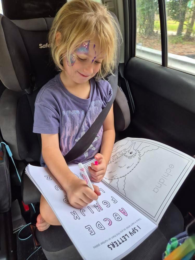 Child sitting in a car seat with a australian road trip coloring book and crayon