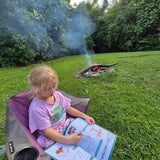 Child sitting in a chair by a campfire in a forest, completing a australian travel journal