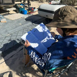 Child sitting outdoors, holding an australian sea life activity book with camping equipment in the background.