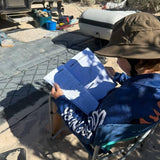Child sitting outdoors, holding an australian sea life activity book with camping equipment in the background.