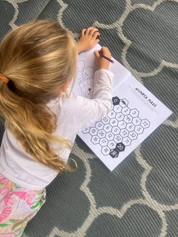 Child coloring a number maze on a  australian activity book with a crayon on a patterned rug.