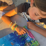 Two children sitting on a beach, one reading a book titled 'Australian Sea Life'.