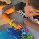 Two children sitting on a beach, one reading a book titled 'Australian Sea Life'.
