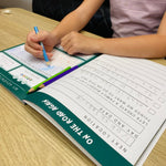 Child writing in an australian travel journal with a pen on a wooden table