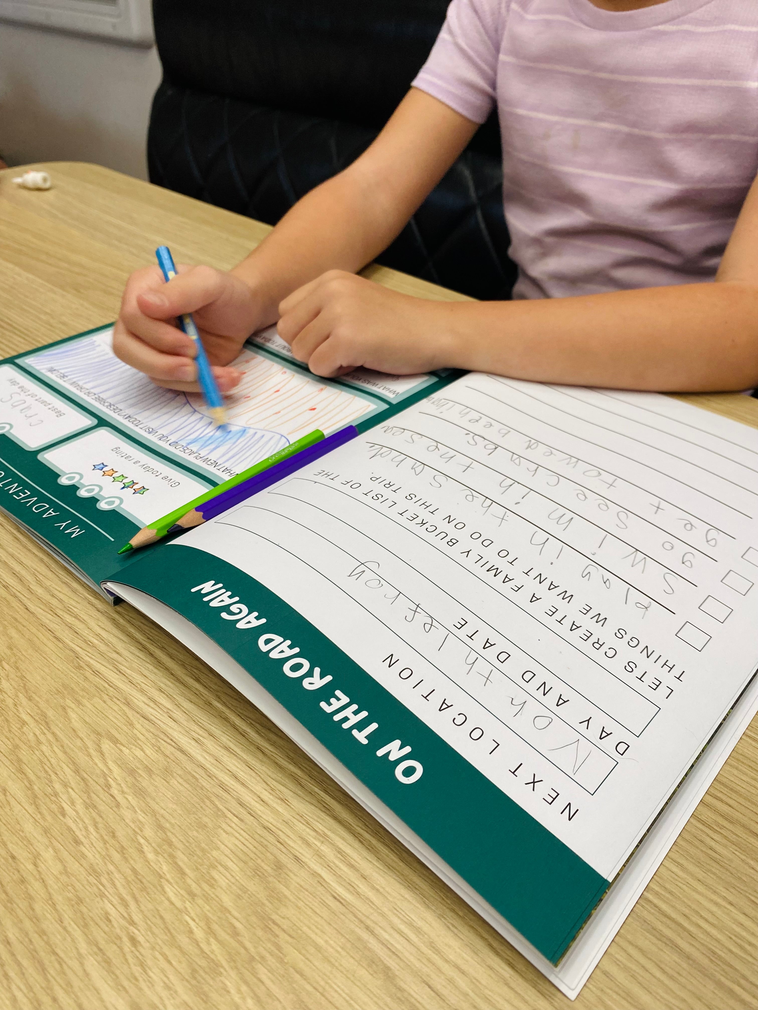 Child writing in an australian travel journal with a pen on a wooden table