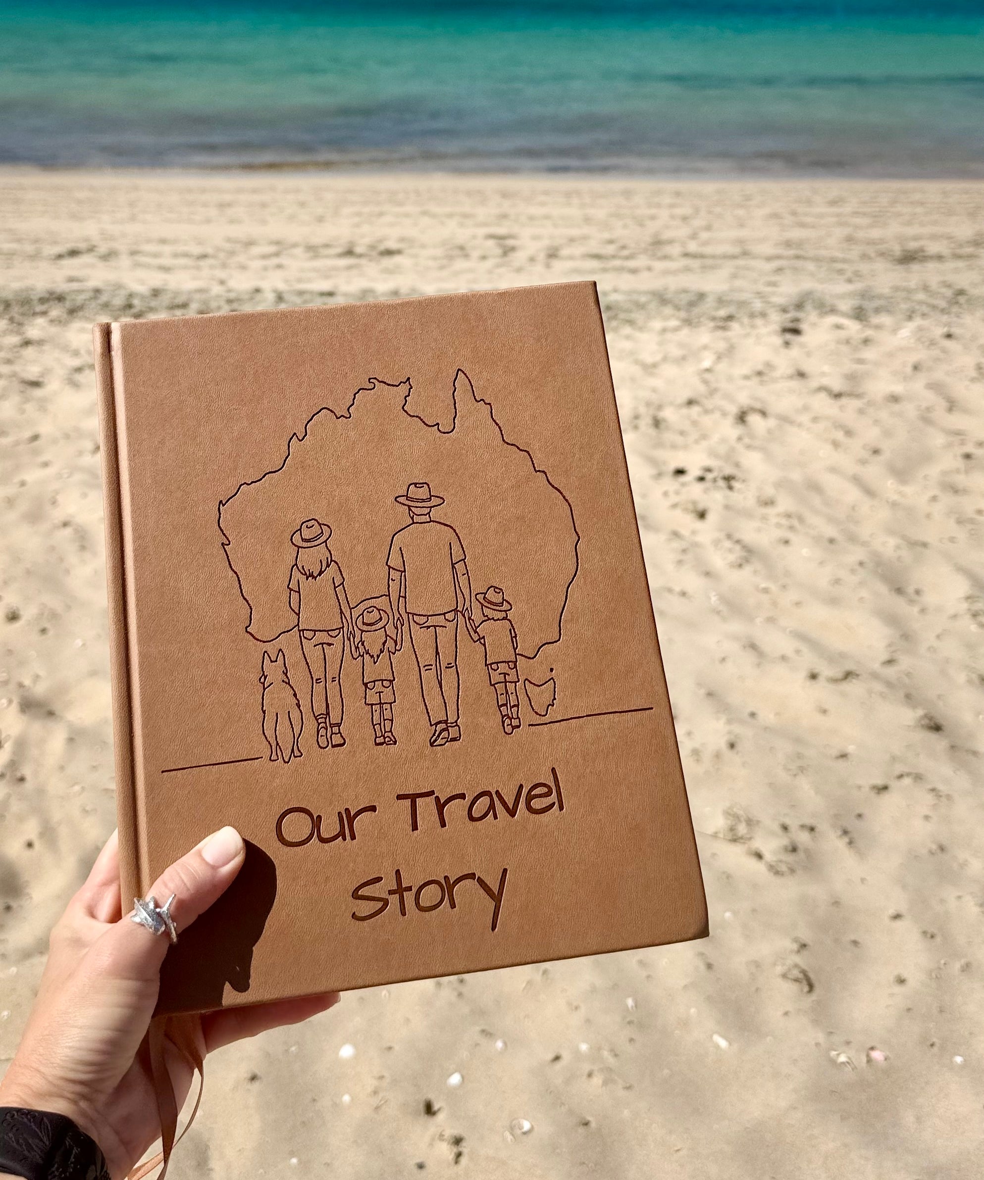 Sand coloured australian travel journal with 'Our Travel Story' text and family illustration held on a beach.