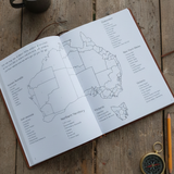 Open book with a map of the Australia broken down into regions, States on a wooden surface with a mug, pencil, and compass.
